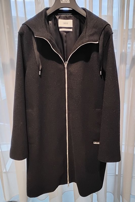 Schwarzer Kapuzenmantel mit silbernem Reißverschluss hängt in einem Geschäft.