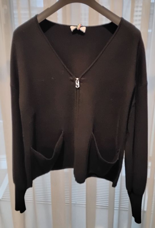Schwarzer Cardigan-Pullover mit Reißverschluss und zwei Vordertaschen, hängt auf einem schwarzen Kleiderbügel.