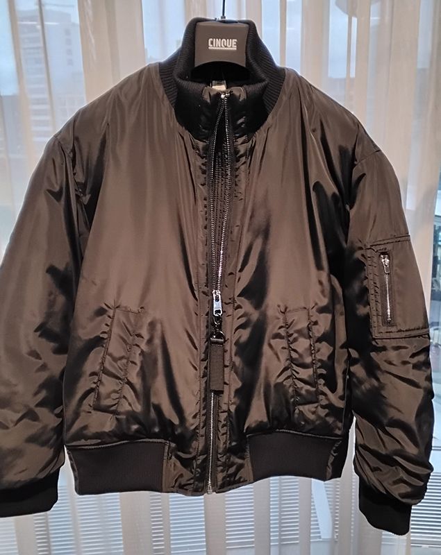 Schwarze Bomberjacke mit gerippten Bündchen und Kragen, hängt drinnen.