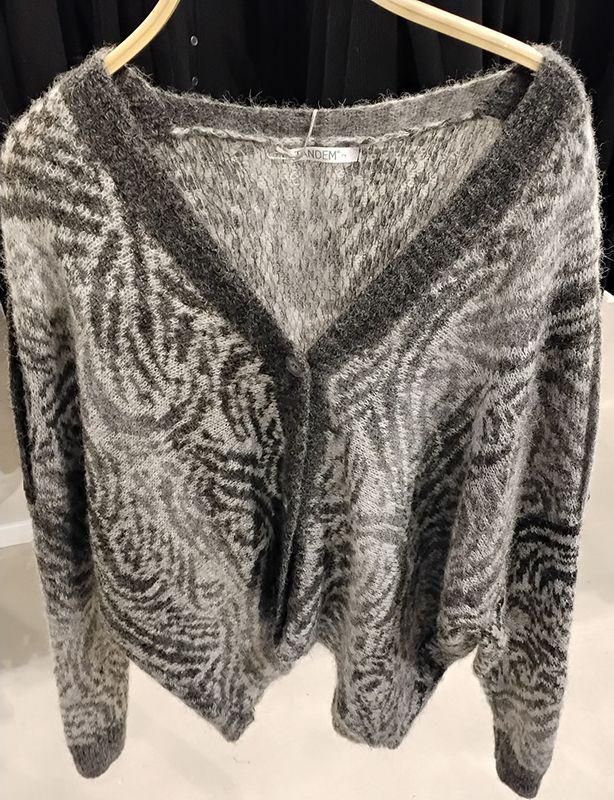 Graue gemusterte Strickjacke an einem Holzkleiderbügel.