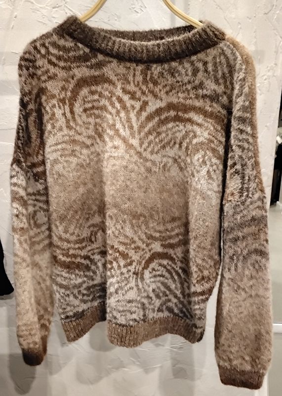 Ein braun-cremefarbener gemusterter Pullover hängt auf einem Kleiderbügel.