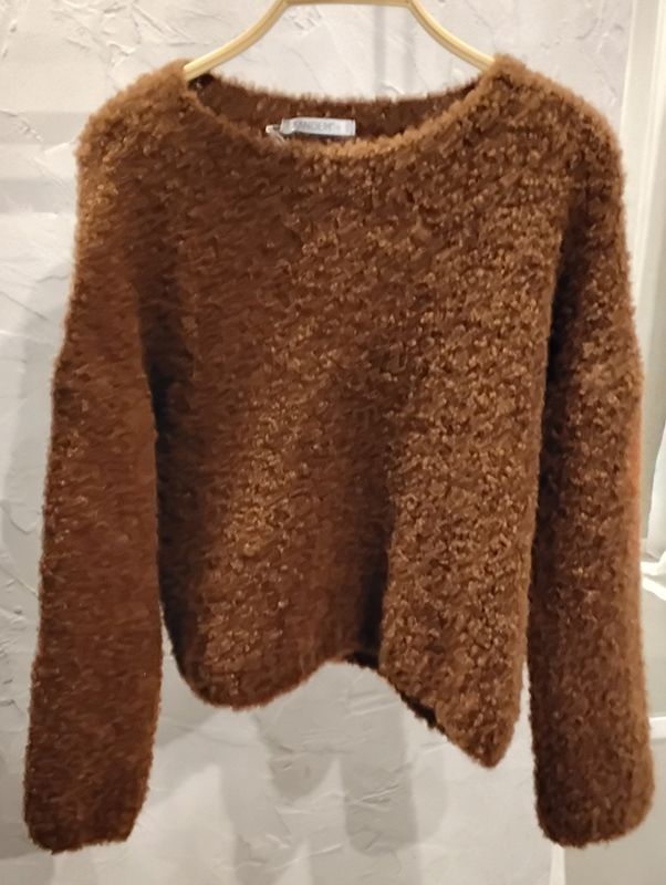 Brauner, flauschiger Rundhalspullover auf einem Kleiderbügel.