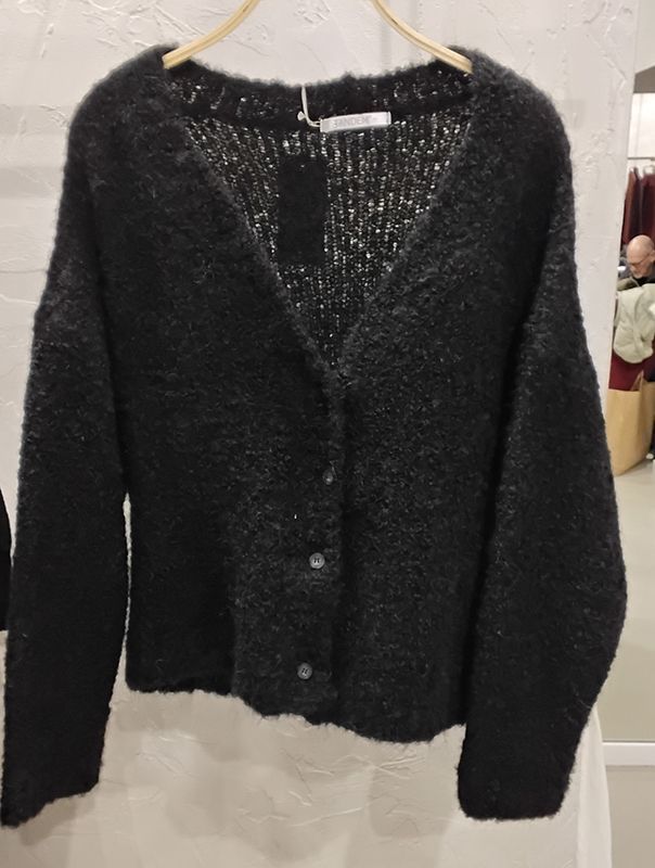 Schwarze, flauschige Strickjacke mit Knöpfen, hängt an einem Holzkleiderbügel.