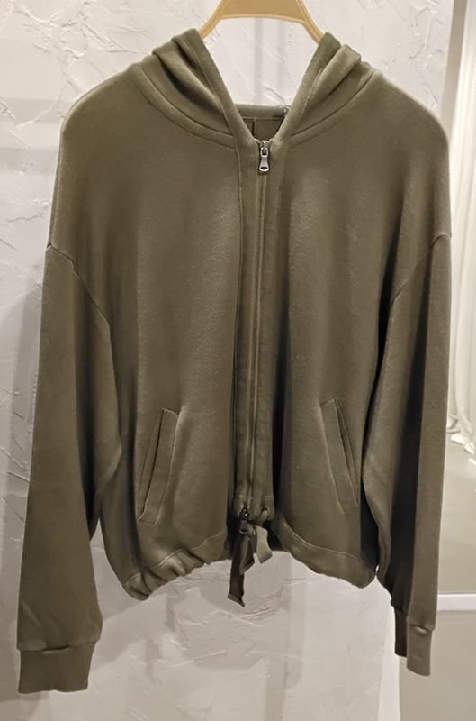 Ein olivgrüner Kapuzenpullover mit Reißverschluss hängt an einem Kleiderständer.