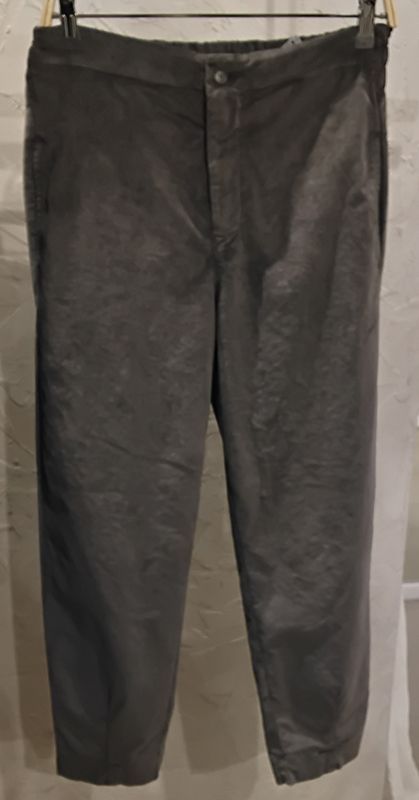 Eine graue Cordhose hängt an einem schwarzen Kleiderbügel vor einer hellgrauen Wand.