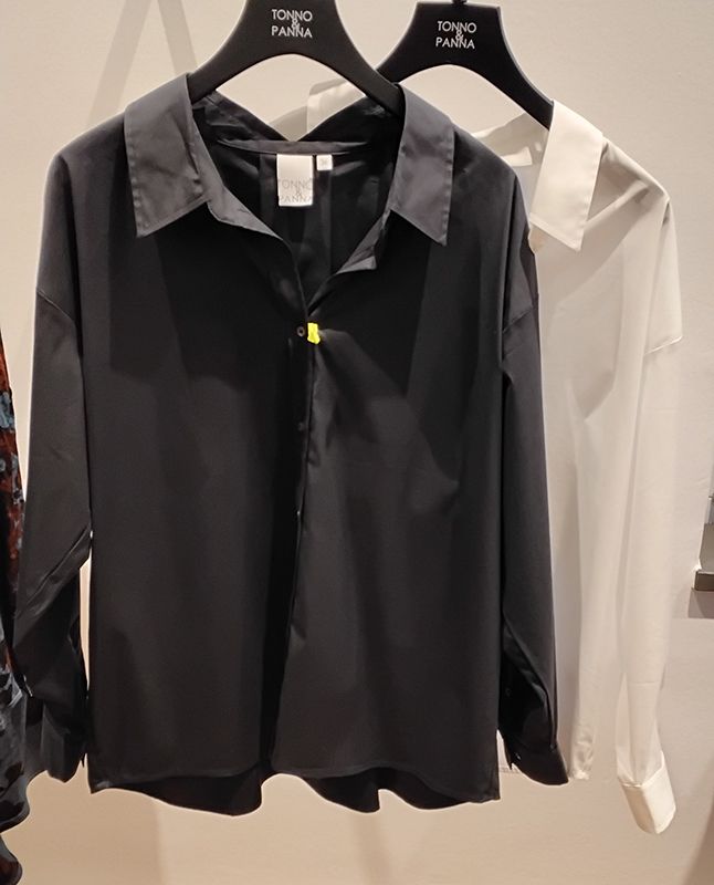 Schwarze und weiße Hemden hängen an einem Kleiderständer. Das schwarze Hemd hat einen einzelnen gelben Knopf.