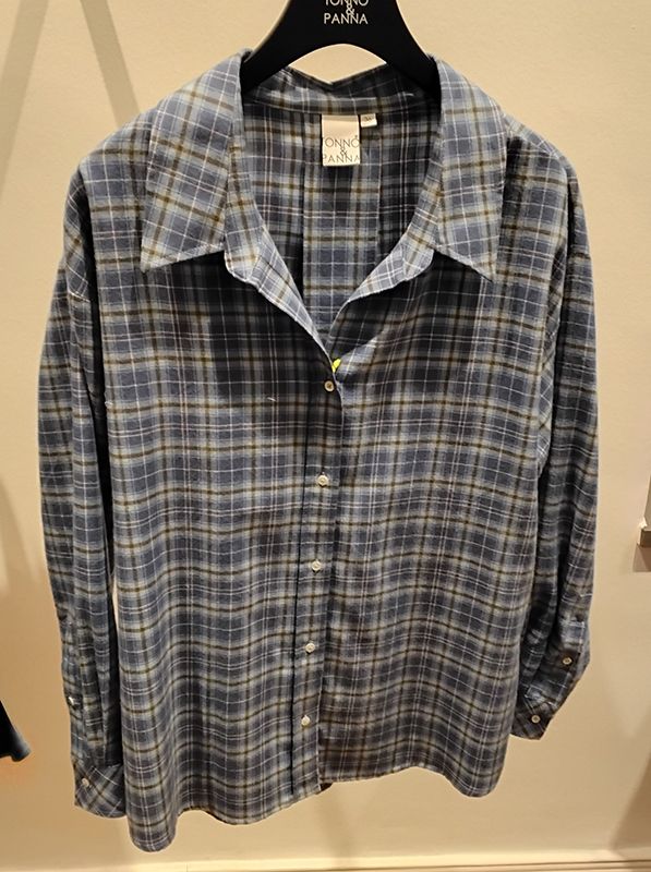 Ein blau kariertes Button-Down-Hemd hängt an einem schwarzen Kleiderbügel vor einer neutralen Wand.