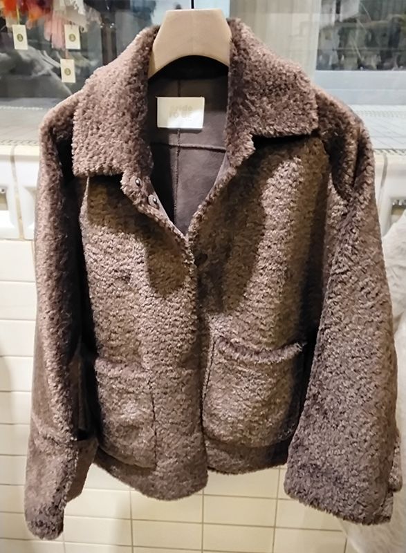 Brauner, flauschiger Mantel auf einem Kleiderbügel, mit Reverskragen und Taschen.