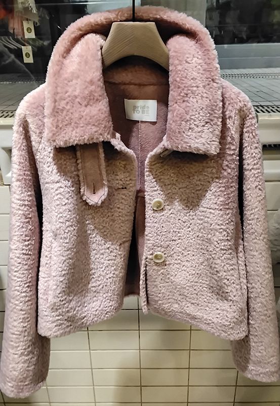 Kurze, pinkfarbene Kunstpelzjacke mit großem Kragen und zwei Knöpfen hängt an einem Kleiderständer.