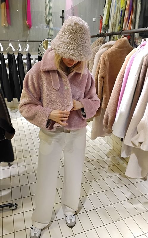 Frau in rosa Teddyjacke und -hut, weiße Hose, in einem Bekleidungsgeschäft.