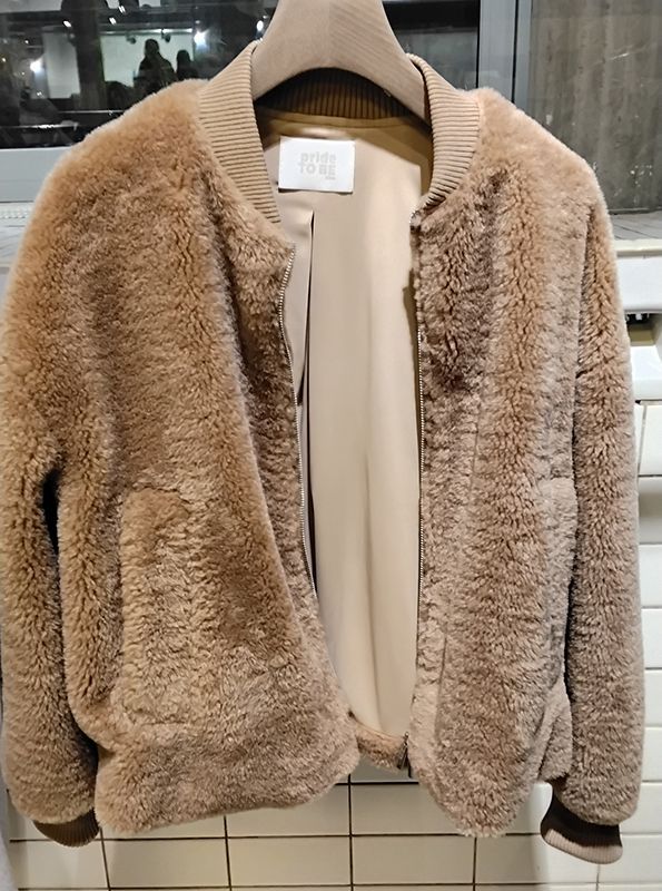 Braune, flauschige Bomberjacke mit cremefarbenem Futter hängt an einem Auslagetisch.