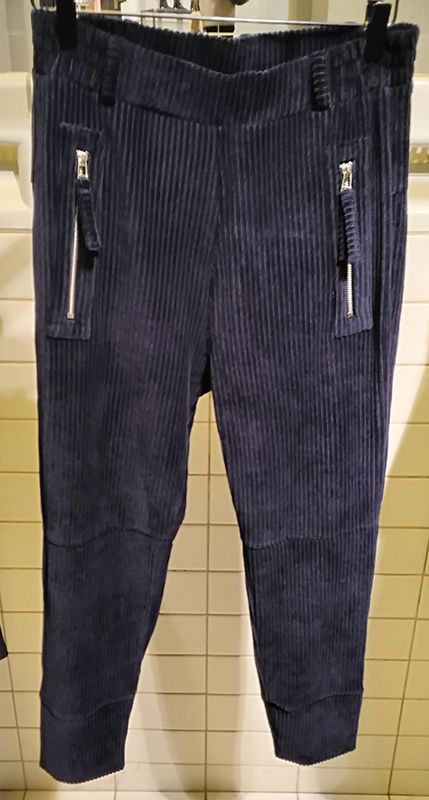 Eine marineblaue Cordhose mit Reißverschlusstaschen hängt vor einer gefliesten Wand.