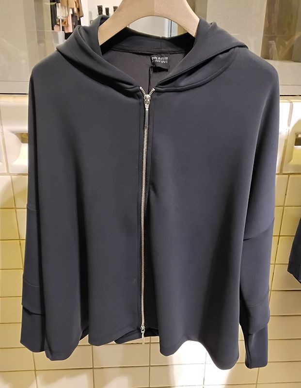 Schwarzer Kapuzenpullover mit Reißverschluss hängt an einem Kleiderständer.