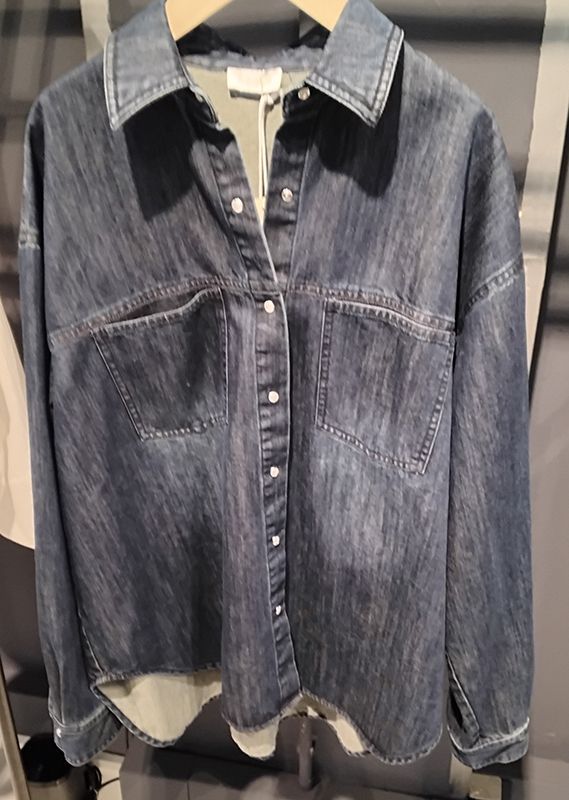 Jeans-Button-Down-Hemd mit zwei Brusttaschen, hängt auf einem Holzbügel.