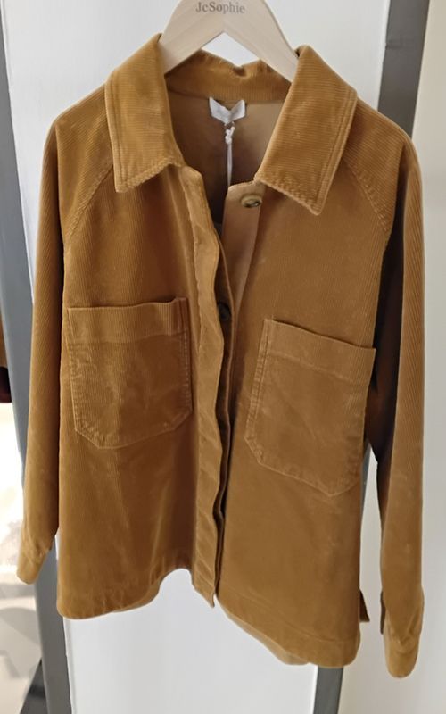 Cordjacke, senfgelb, mit großen Taschen und Kragen, hängt auf einem Holzbügel.