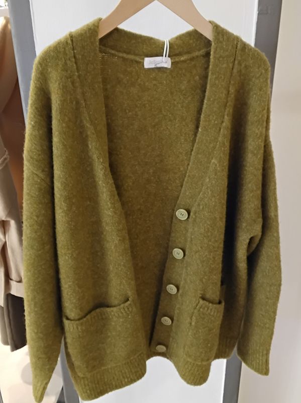 Olivgrüne Strickjacke mit großen Knöpfen, hängt auf einem Holzbügel.