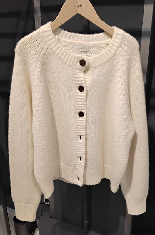 Cremefarbene Strickjacke zum Zuknöpfen auf einem Holzbügel.