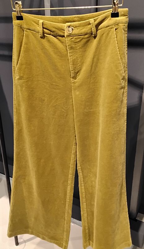 Olivgrüne Cordhosen hängen an einem Ständer.