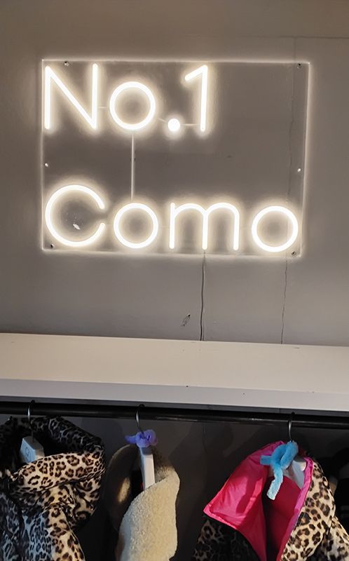 Neonschild „No. 1 Como“ über einem Kleiderständer mit Mänteln in einem Geschäft.