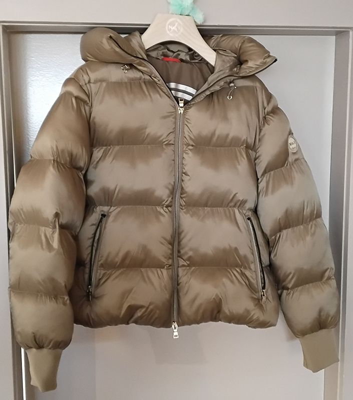 Hellbraune Pufferjacke mit Kapuze hängt in einem Raum.