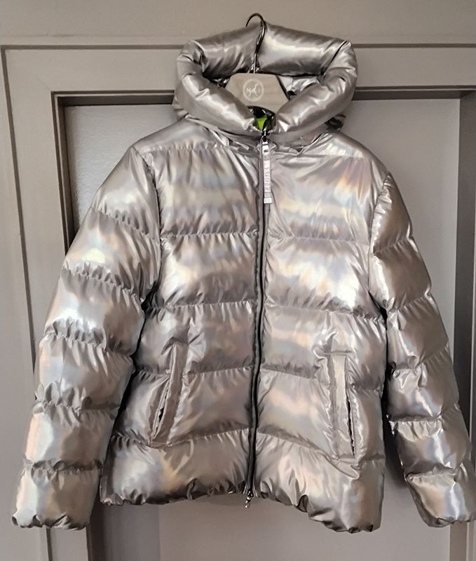Glänzende silberne Pufferjacke mit Kapuze, die an einer Tür hängt.