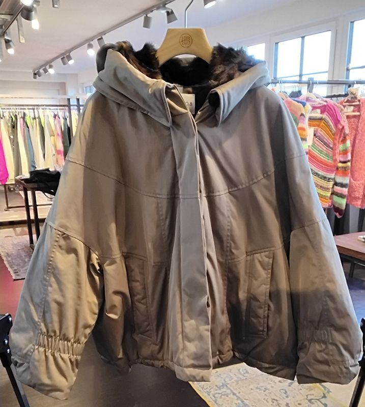 Ein hellbrauner Wintermantel mit Kapuze und Pelzfutter hängt in einem Bekleidungsgeschäft.