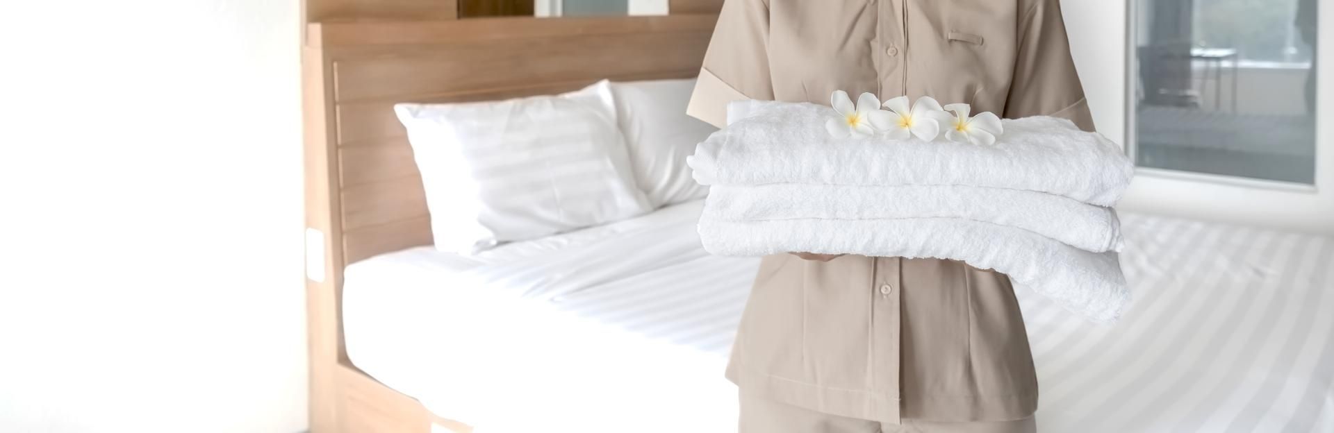 Ein frischbezogenes Bett, eine Person bringt gerade neue Handtücher in den Raum