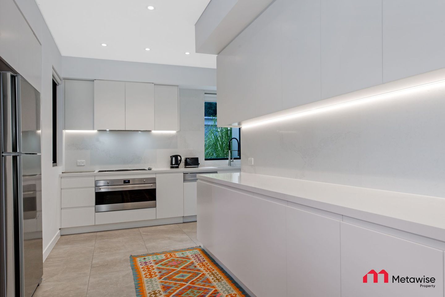 A kitchen with white cabinets and stainless steel appliances and a rug on the floor.