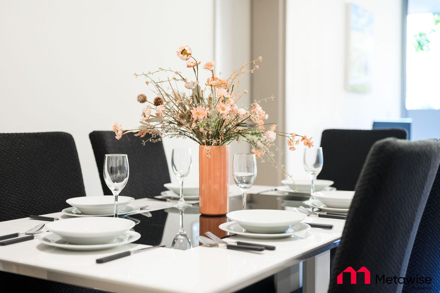 A dining room table with plates , glasses , and a vase of flowers on it.