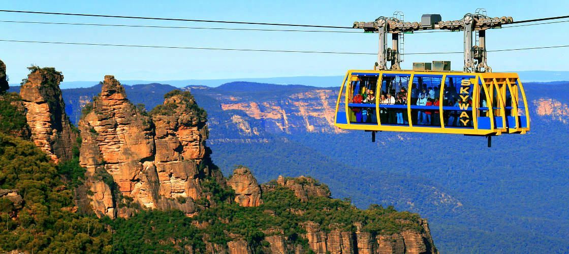 A yellow cable car is flying over a mountain.