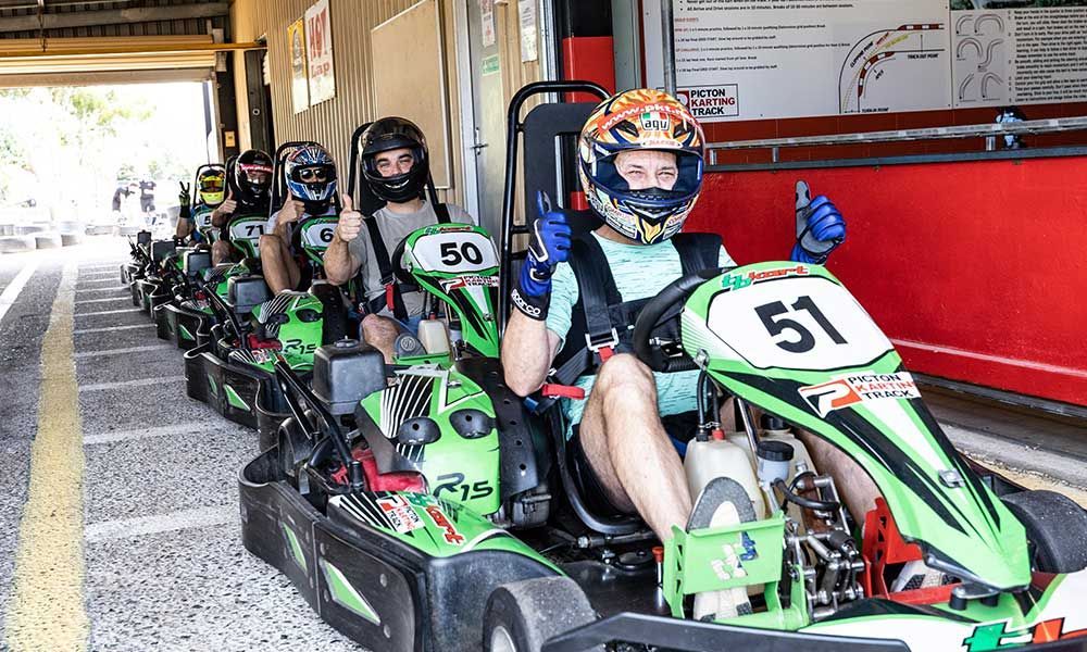 A group of people are riding go karts and giving a thumbs up.