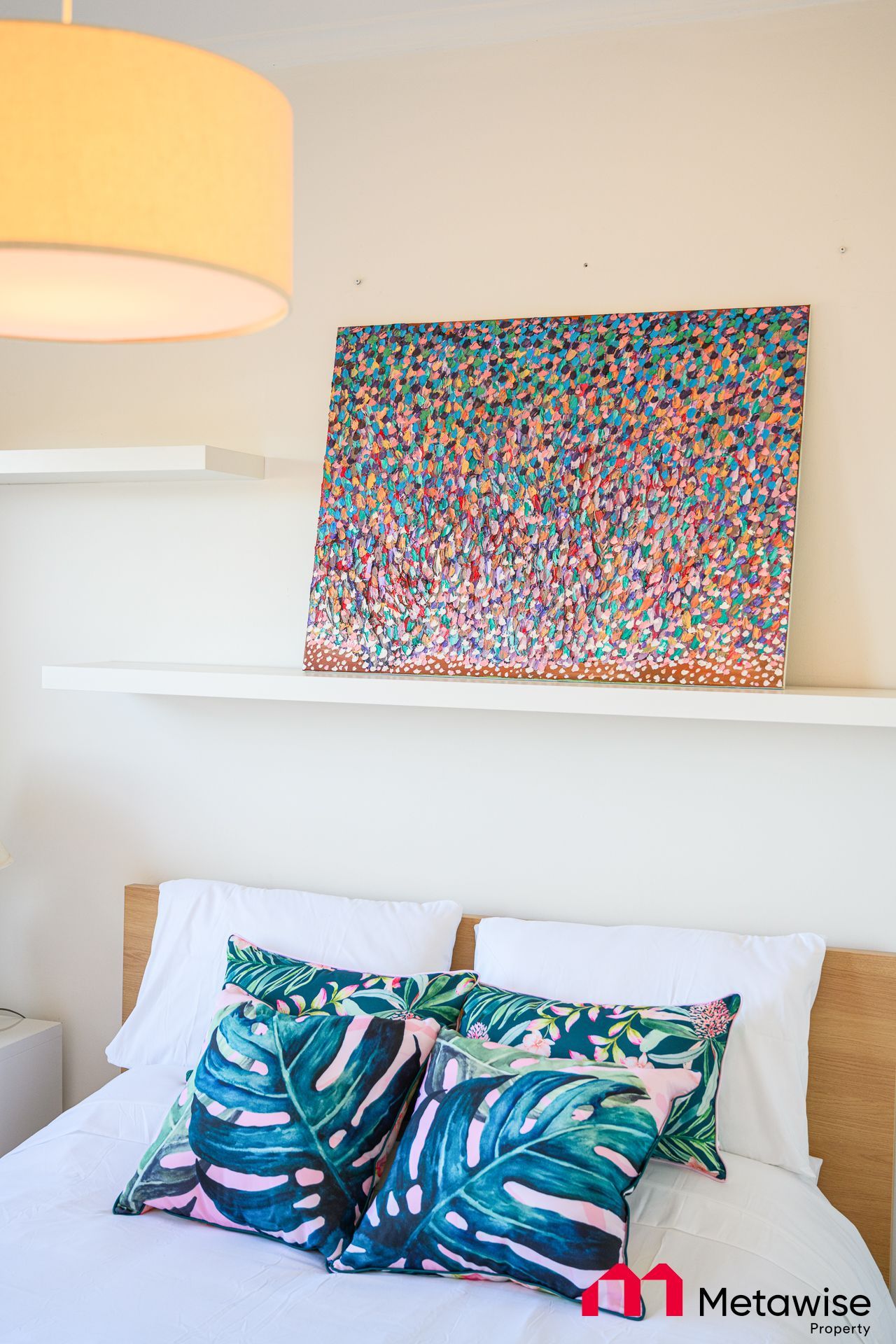 A bed with pillows and a painting on the wall above it.