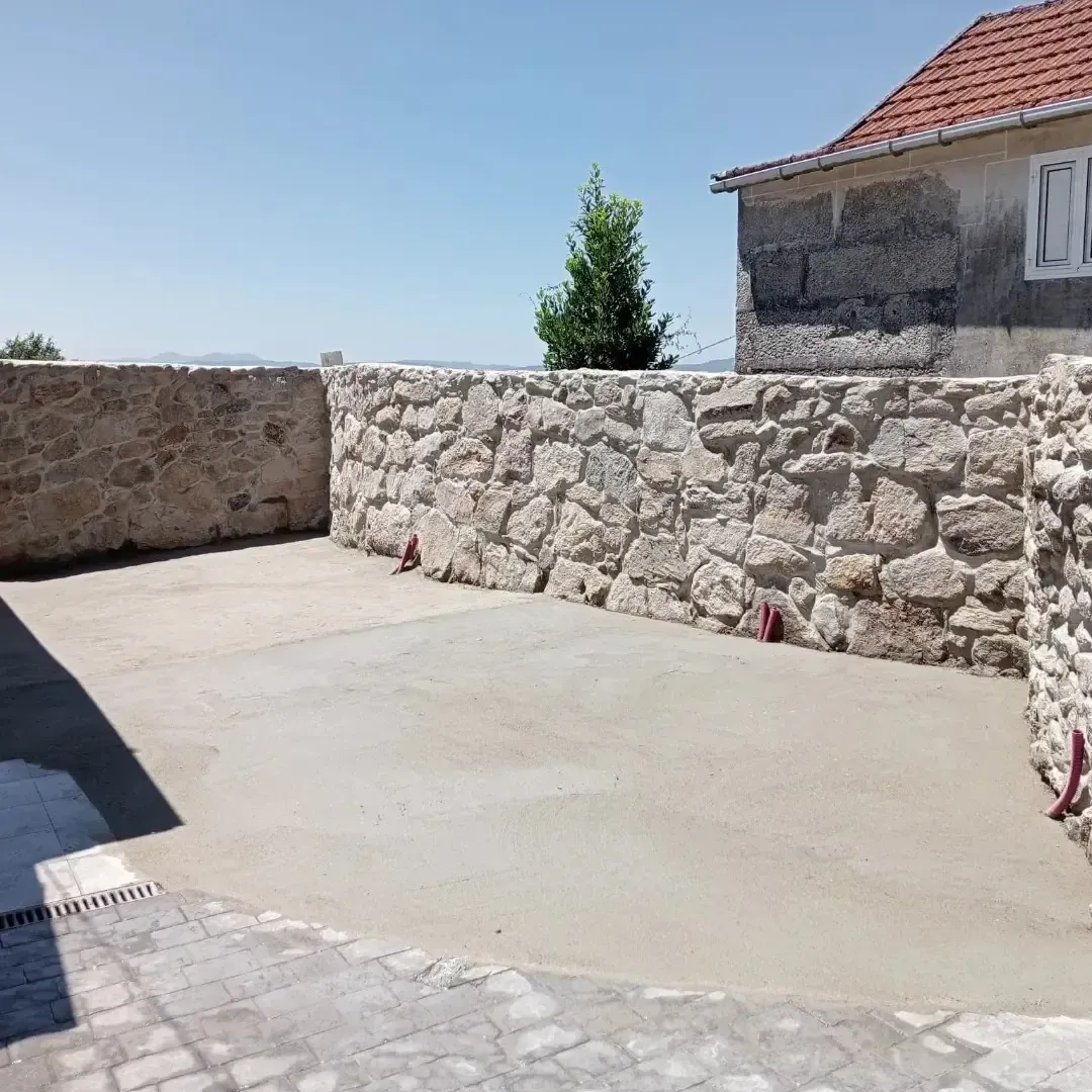 Un patio con muros de piedra y un suelo de hormigón liso bajo un cielo azul despejado.