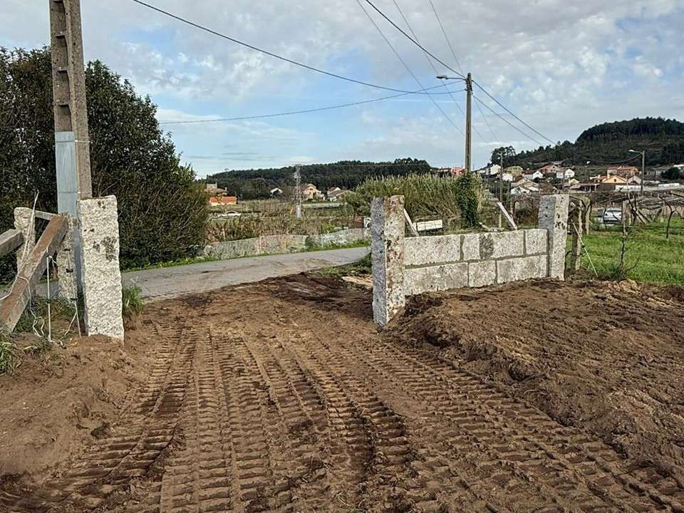 Una puerta de piedra da acceso desde un camino de tierra con huellas 