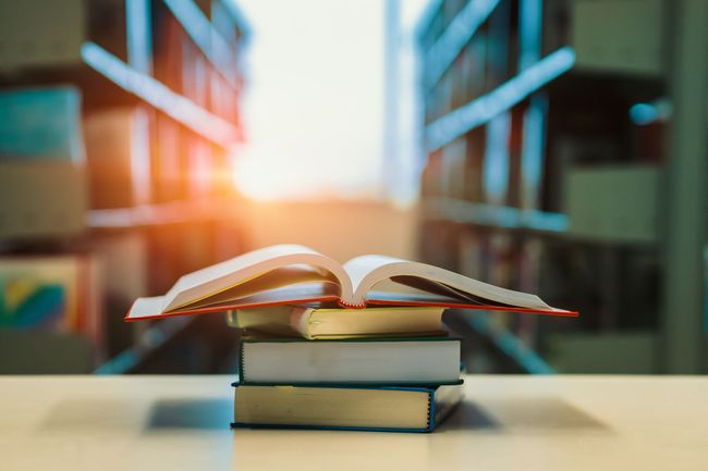 Una pila de libros colocados uno encima del otro sobre una mesa en una biblioteca.