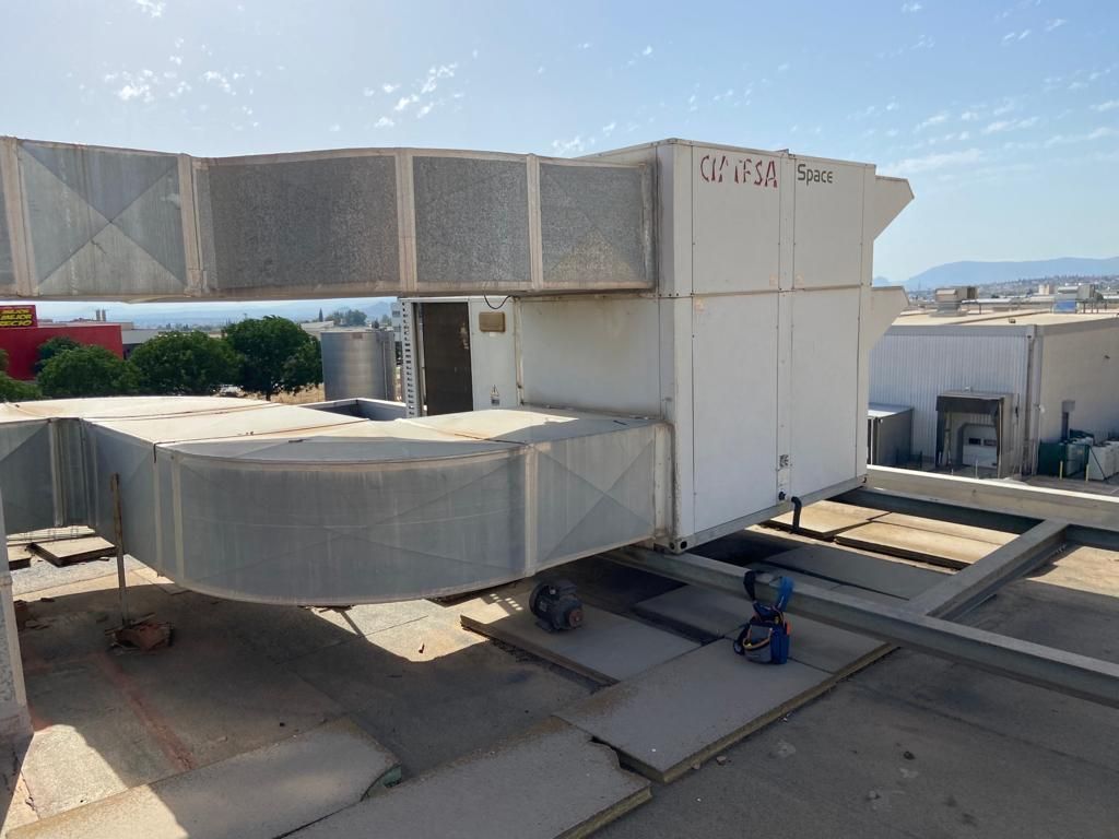 Unidad HVAC en una azotea con conductos, respiraderos y una estructura de soporte, bajo un cielo azul brillante.