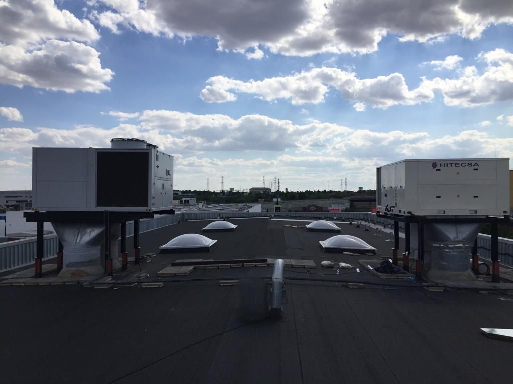 Azotea con dos grandes unidades de climatización sobre soportes elevados. Se ven claraboyas y un cielo azul nublado.