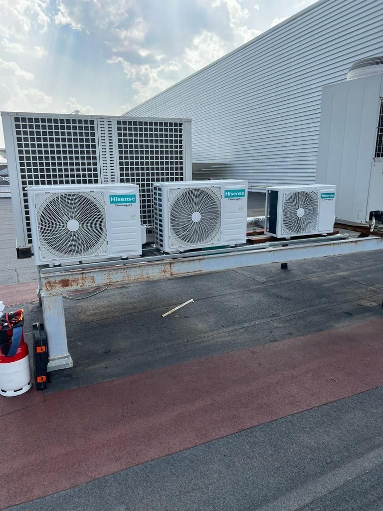 Tres unidades de aire acondicionado sobre una plataforma en la azotea, con una pared blanca enrejada detrás de ellas.