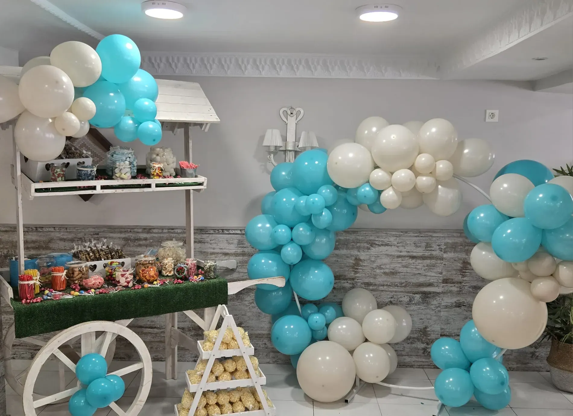 Carrito de dulces decorado con globos azules y blancos, arco y golosinas.