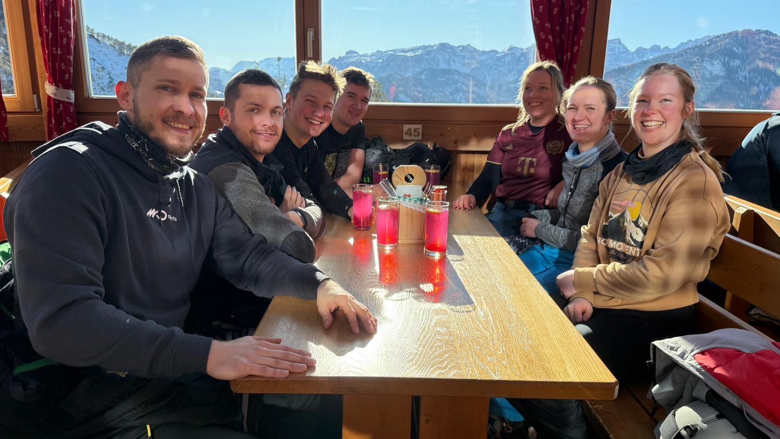 Eine Gruppe von Menschen sitzt an einem Tisch, im Hintergrund sind Berge zu sehen.