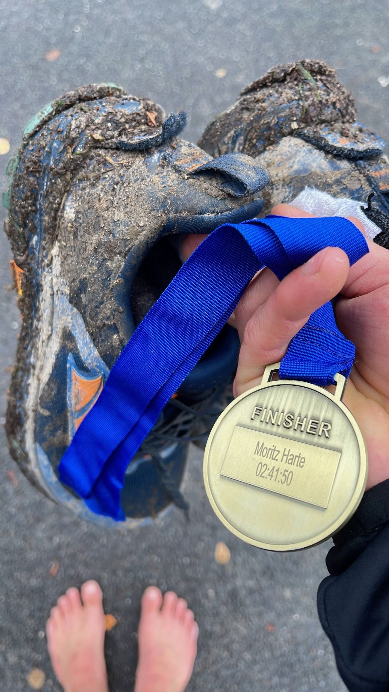 Eine Person hält eine Medaille vor einem schlammigen Schuh.