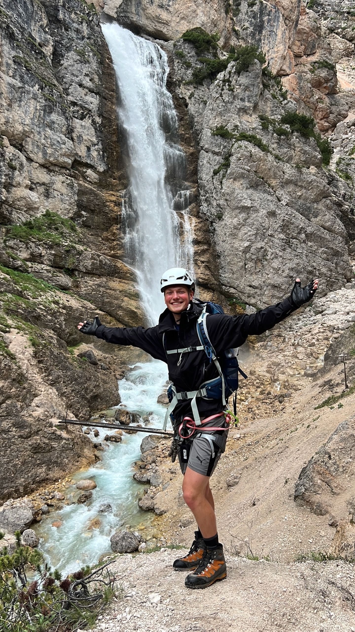 Ein Mann steht mit ausgestreckten Armen vor einem Wasserfall.