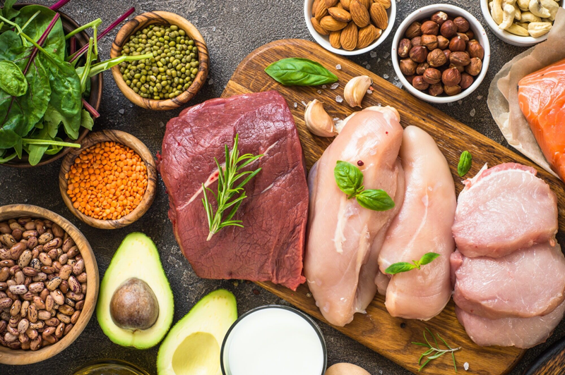 Ein hölzernes Schneidebrett mit Fleisch, Avocado, Nüssen und anderen Lebensmitteln.