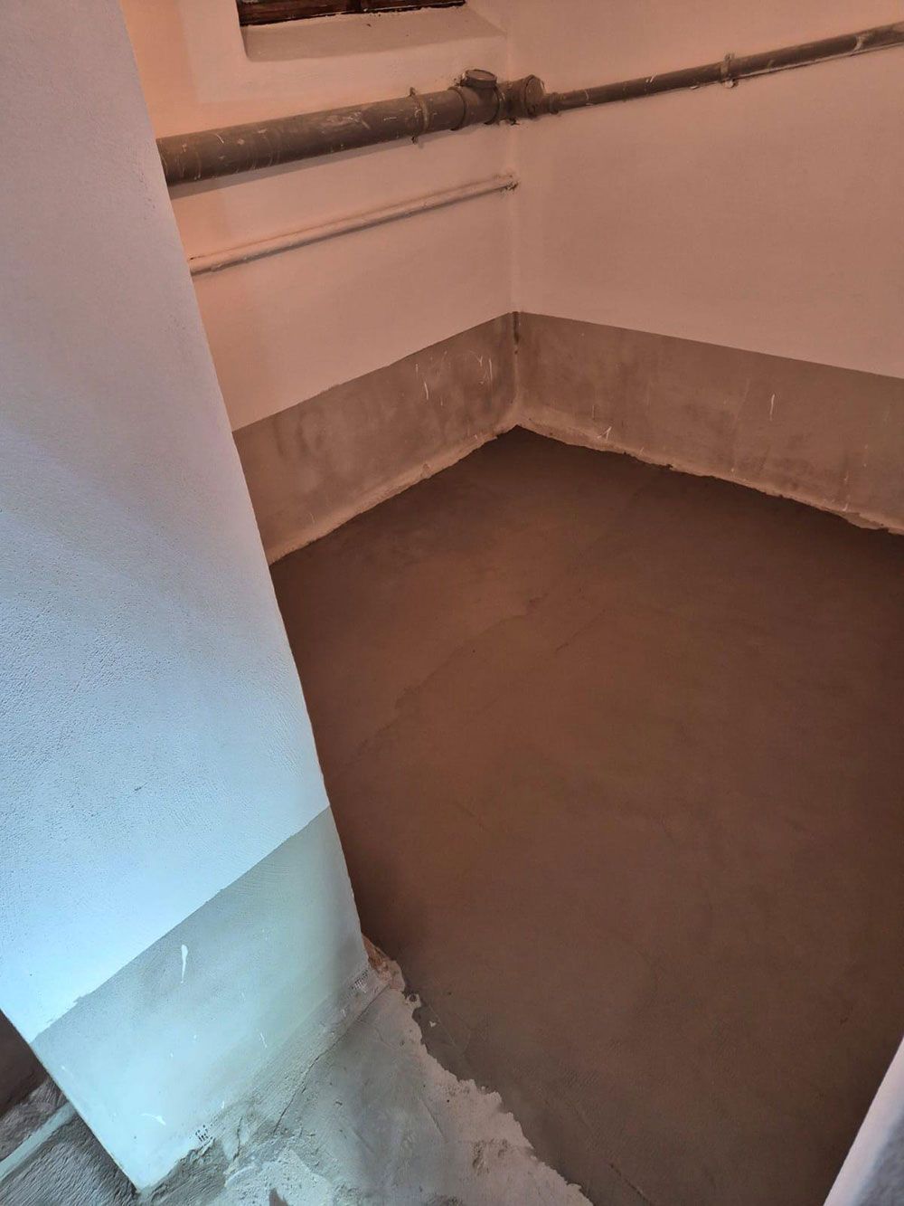 Ein frisch zementierter, brauner Boden in einem Raum mit weißen Wänden, wahrscheinlich einem Keller oder Hauswirtschaftsraum.