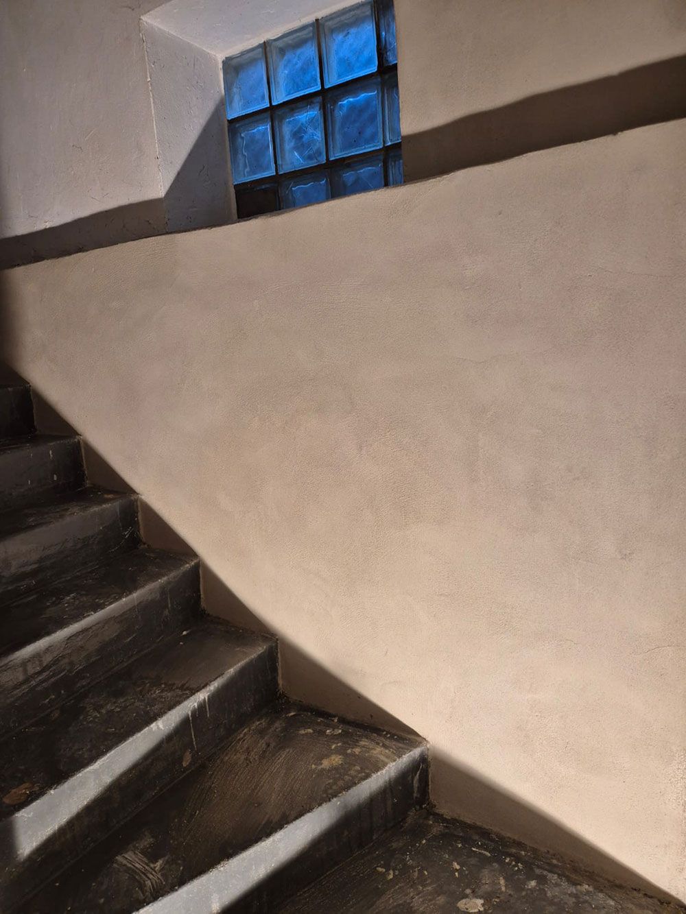 Treppe mit einer Wand, die oben ein blaues Glasbausteinfenster aufweist.