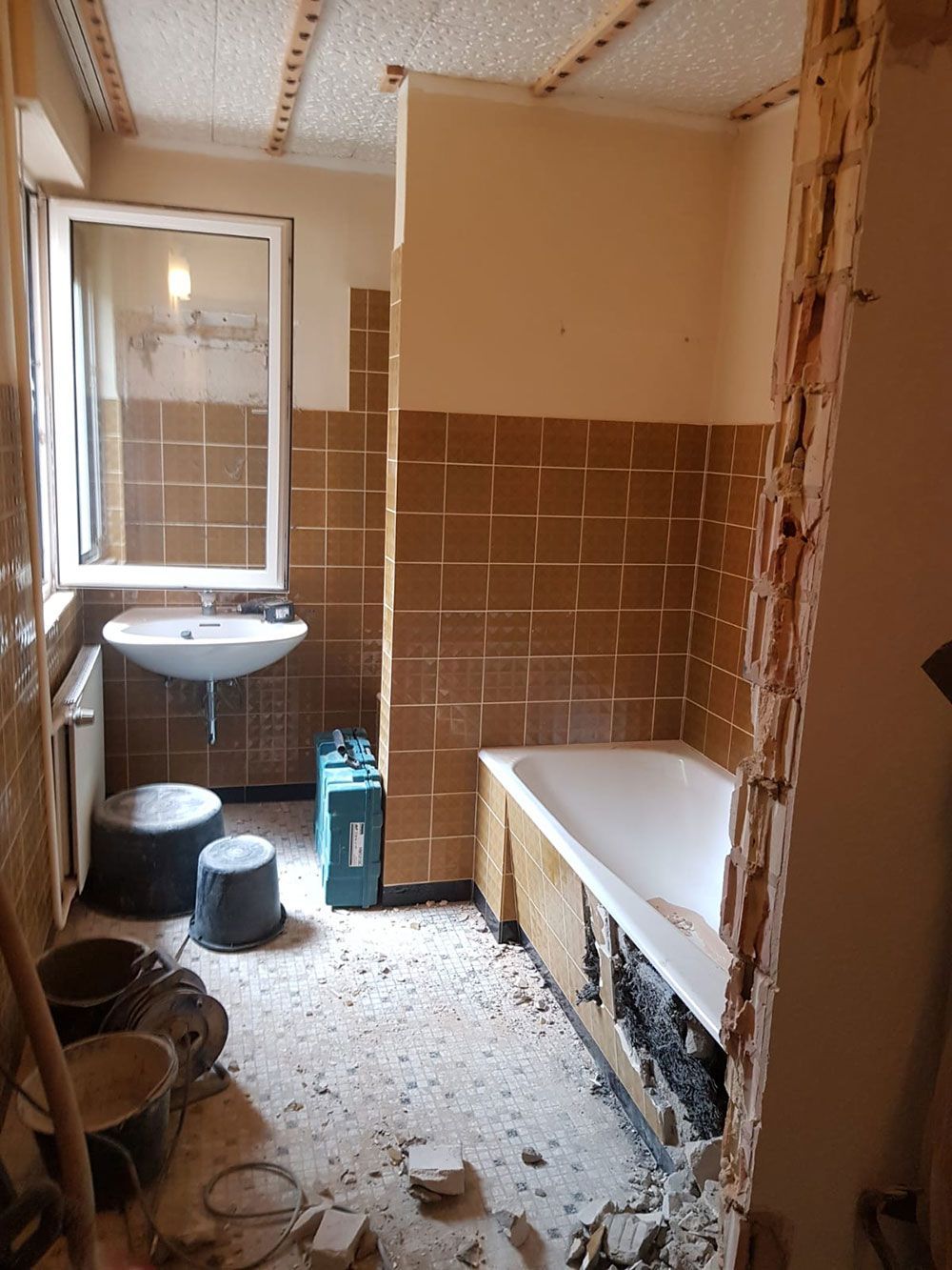 Badezimmerrenovierung im Gange mit braunen Fliesenwänden und freiliegenden Strukturelementen.