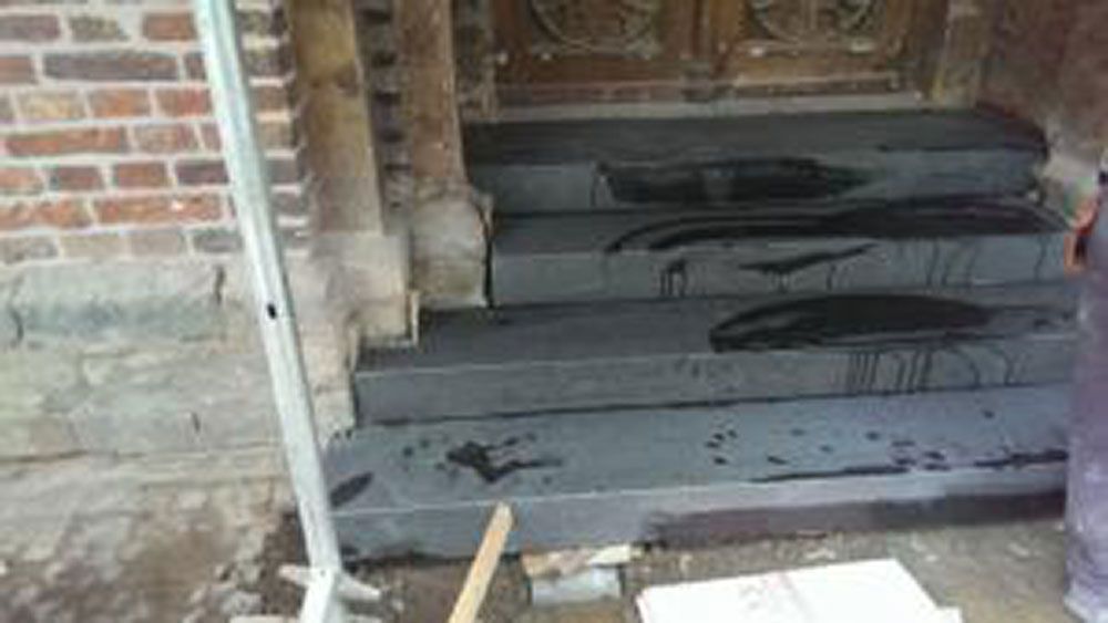 Eingang eines Backsteingebäudes mit dunklen Steinstufen; nass von schwarzer Flüssigkeit.