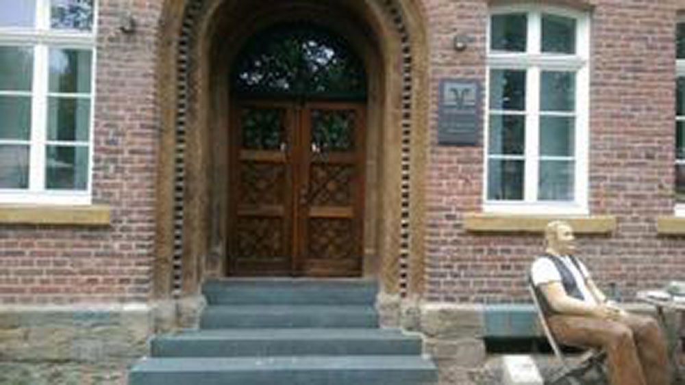 Eingang eines Backsteingebäudes mit Holztüren und einer sitzenden Statue.