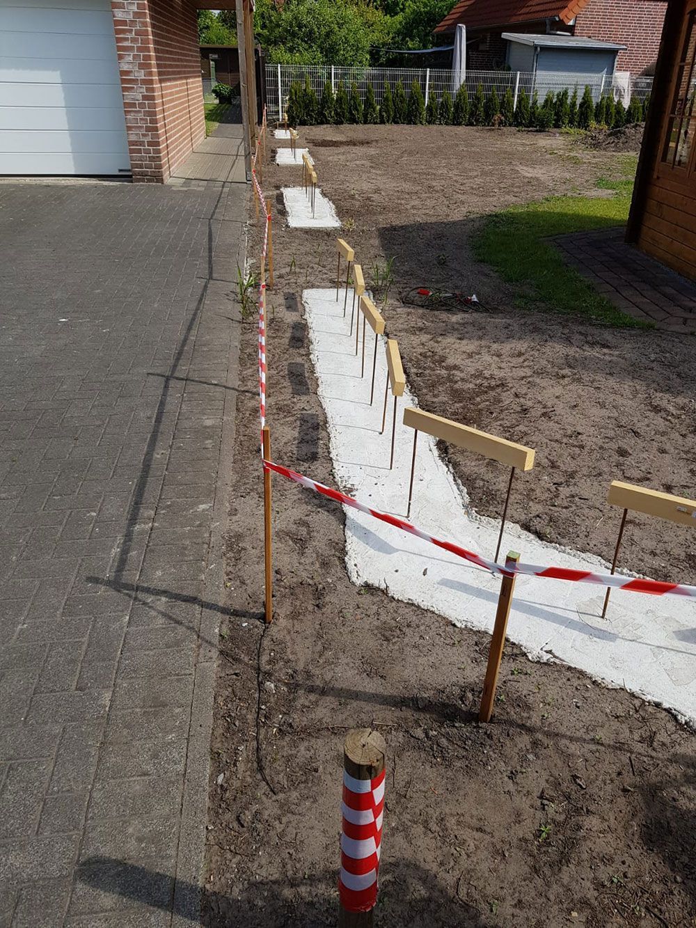 Baustelle mit einer Reihe von Pfählen, die einen Weg markieren, mit Warnband und einem weißen Stoff, der den Boden bedeckt.