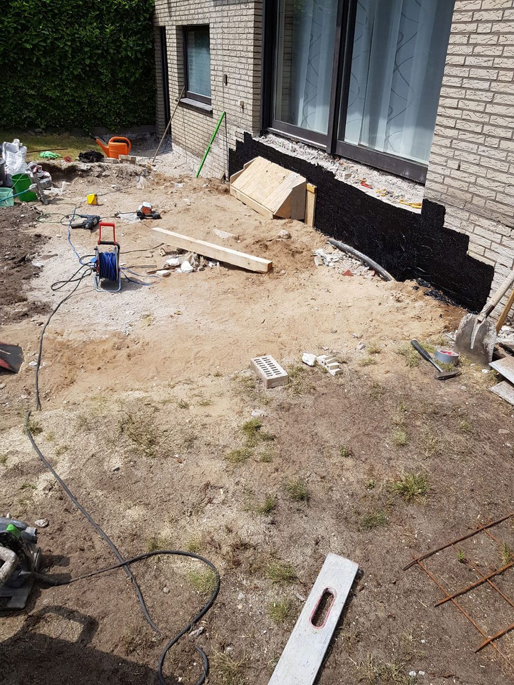 Baustelle: Außenansicht eines Backsteingebäudes mit Aushubfläche, Werkzeug und freiliegendem Fundament.